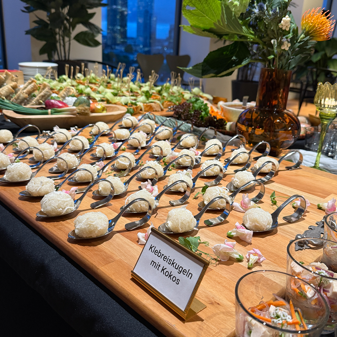 Ein Buffet mit Klebreiskugeln in Löffeln, umgeben von Blumen und weiteren gesunden Speisen.